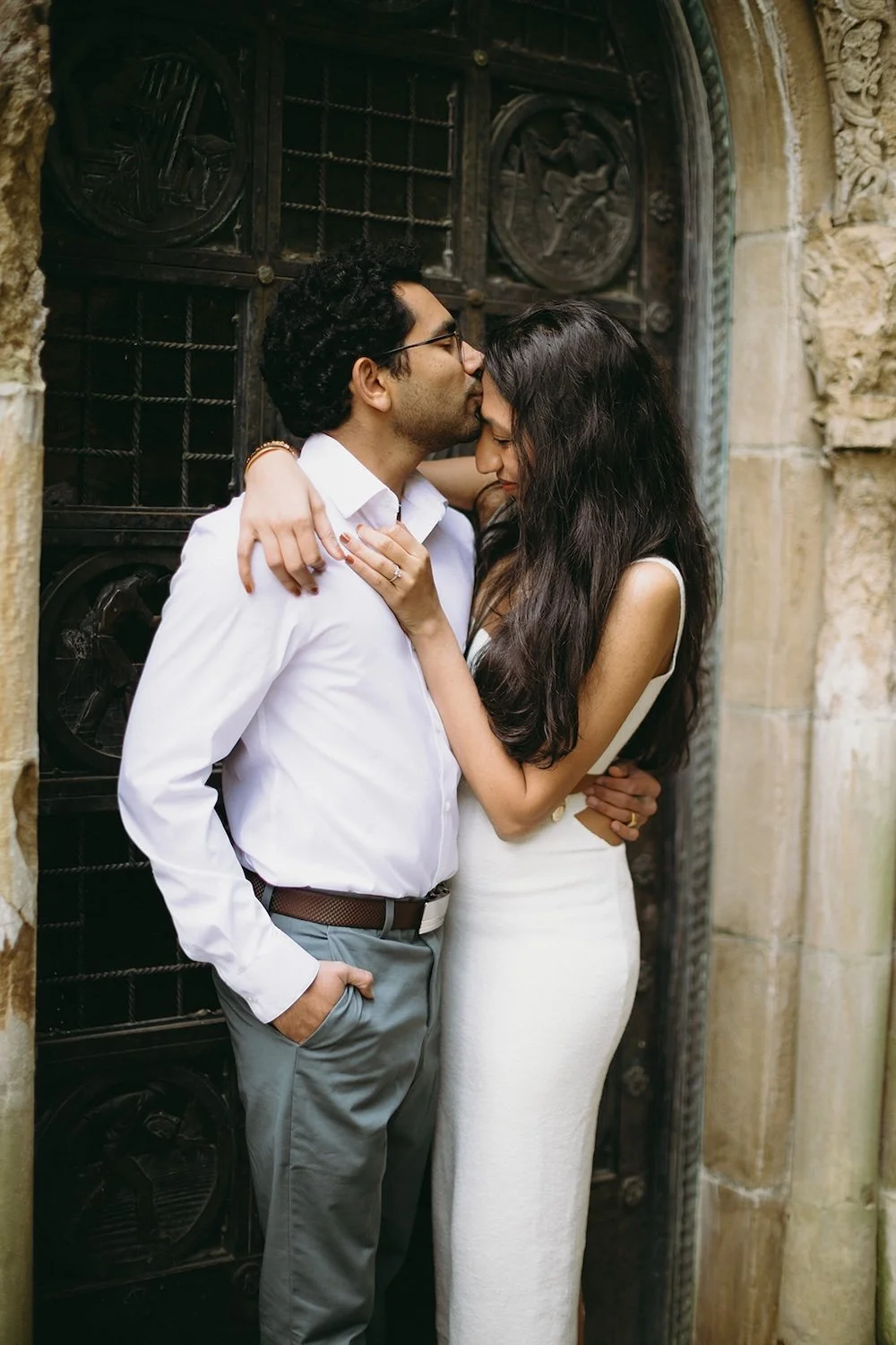 The future groom kisses her forehead in the antique doorway. 