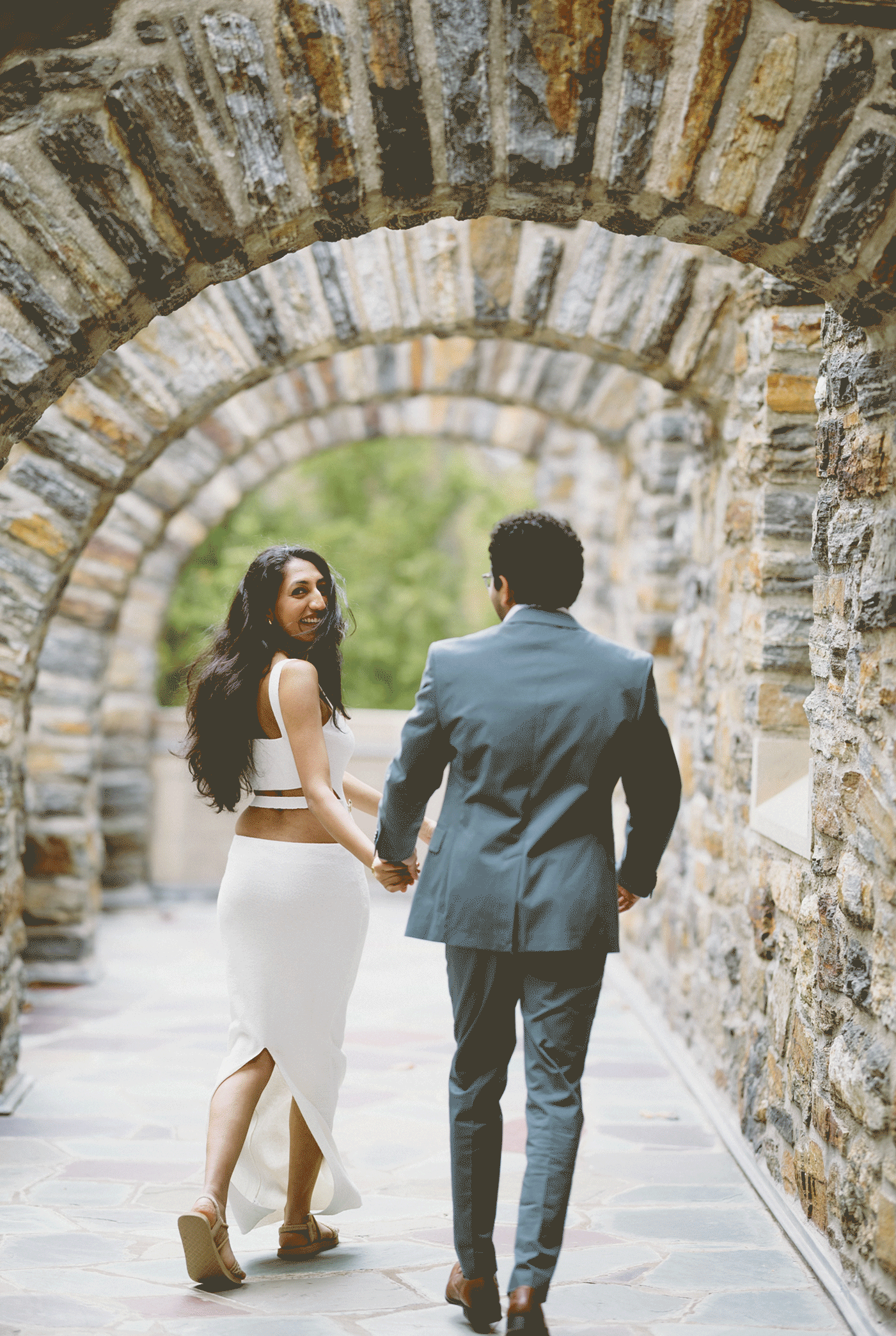 The couple run through the arches smiling and holding hands. 