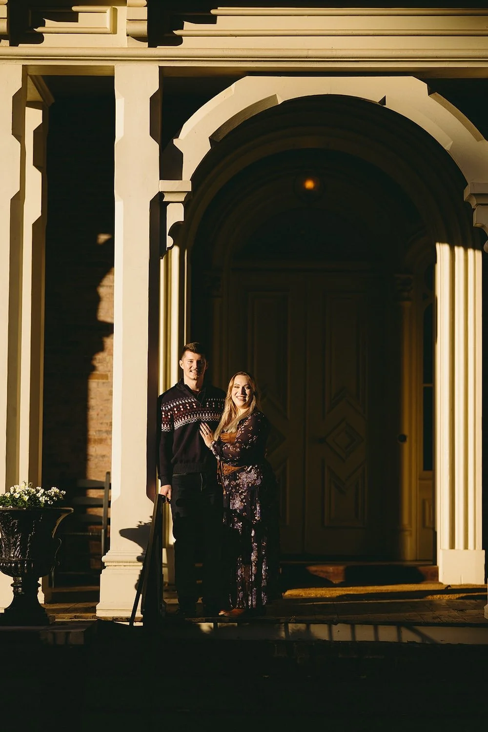 The couple hold one another close as they lean against the post of the historic building 