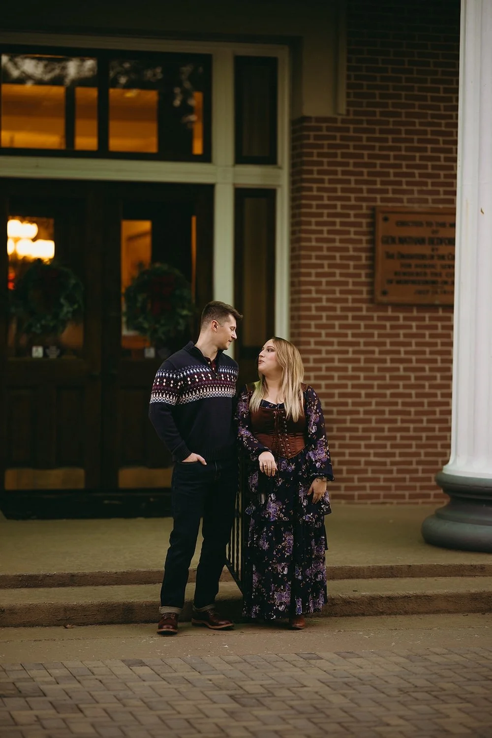 The couple pose together on the porch of the Christmas decorated courthouse building. 
