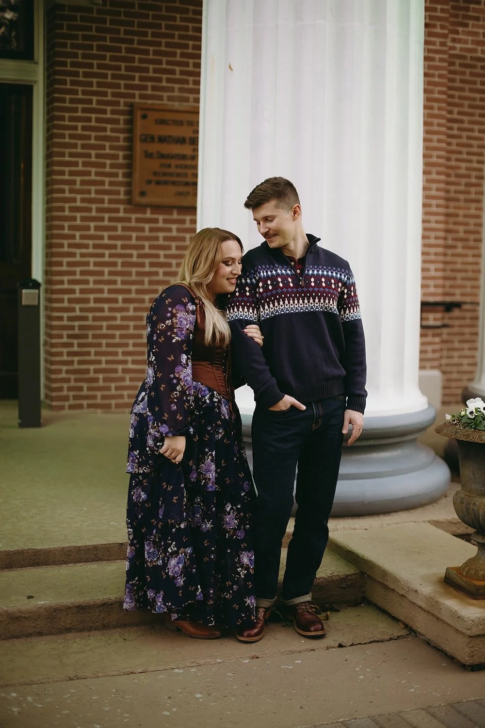 The future bride holds her groom close while standing infront of their courthouse building.