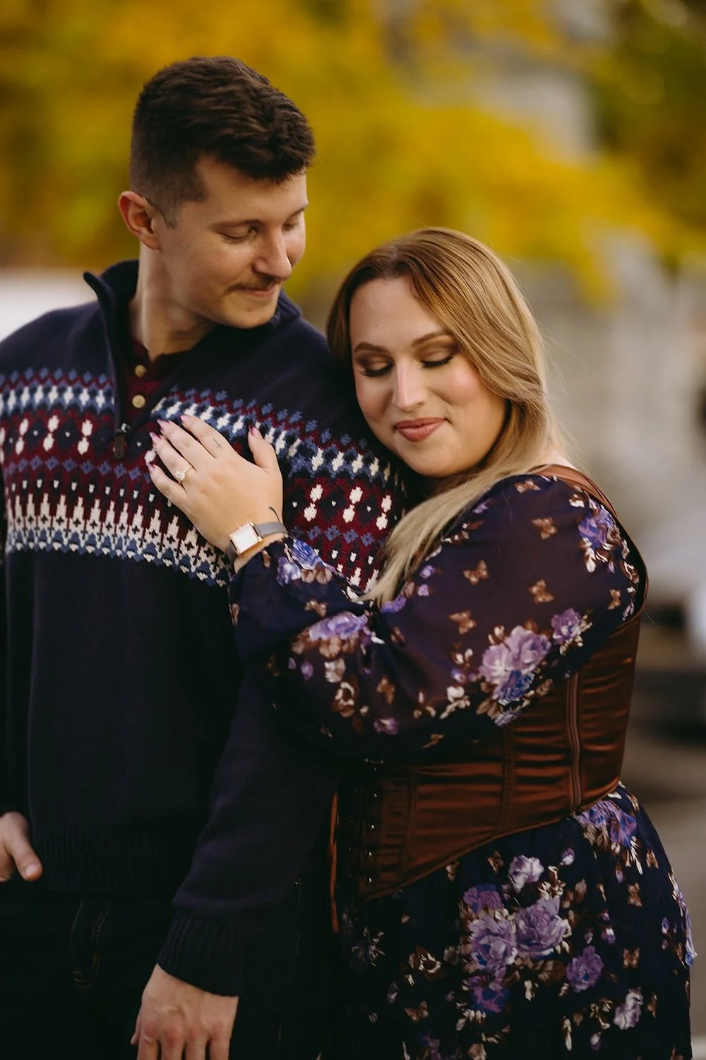 The future bride rests her head on the shoulder of her groom with her hand resting on his chest. The engagement ring shining bright on his chest. 
