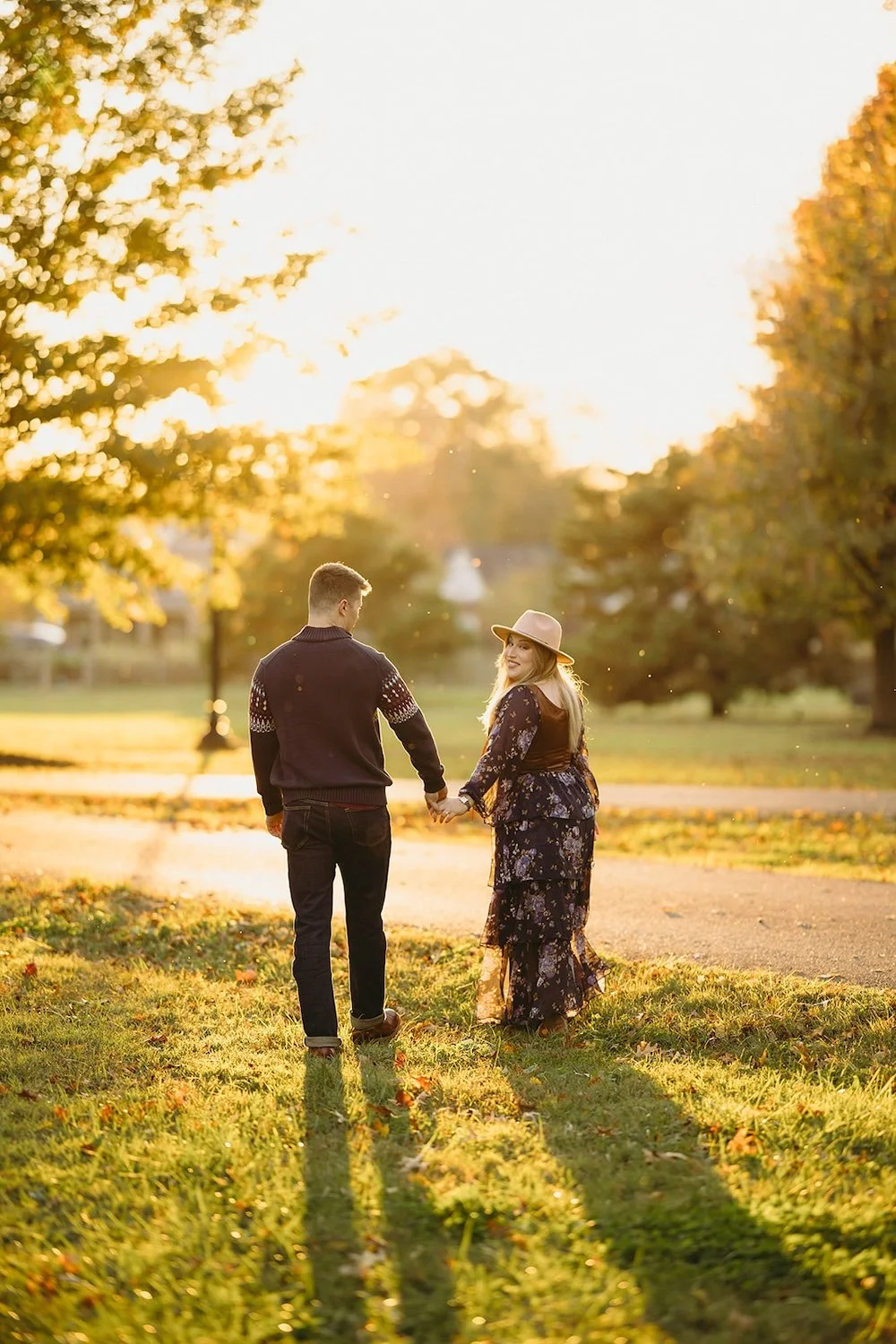 The couple walk hand-in-hand toward the walking path with the sun shining down on them. 