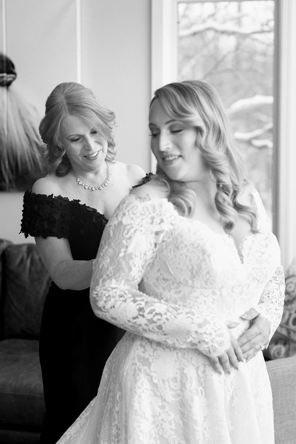 Black and white photo of family buttoning the brides wedding dress. 