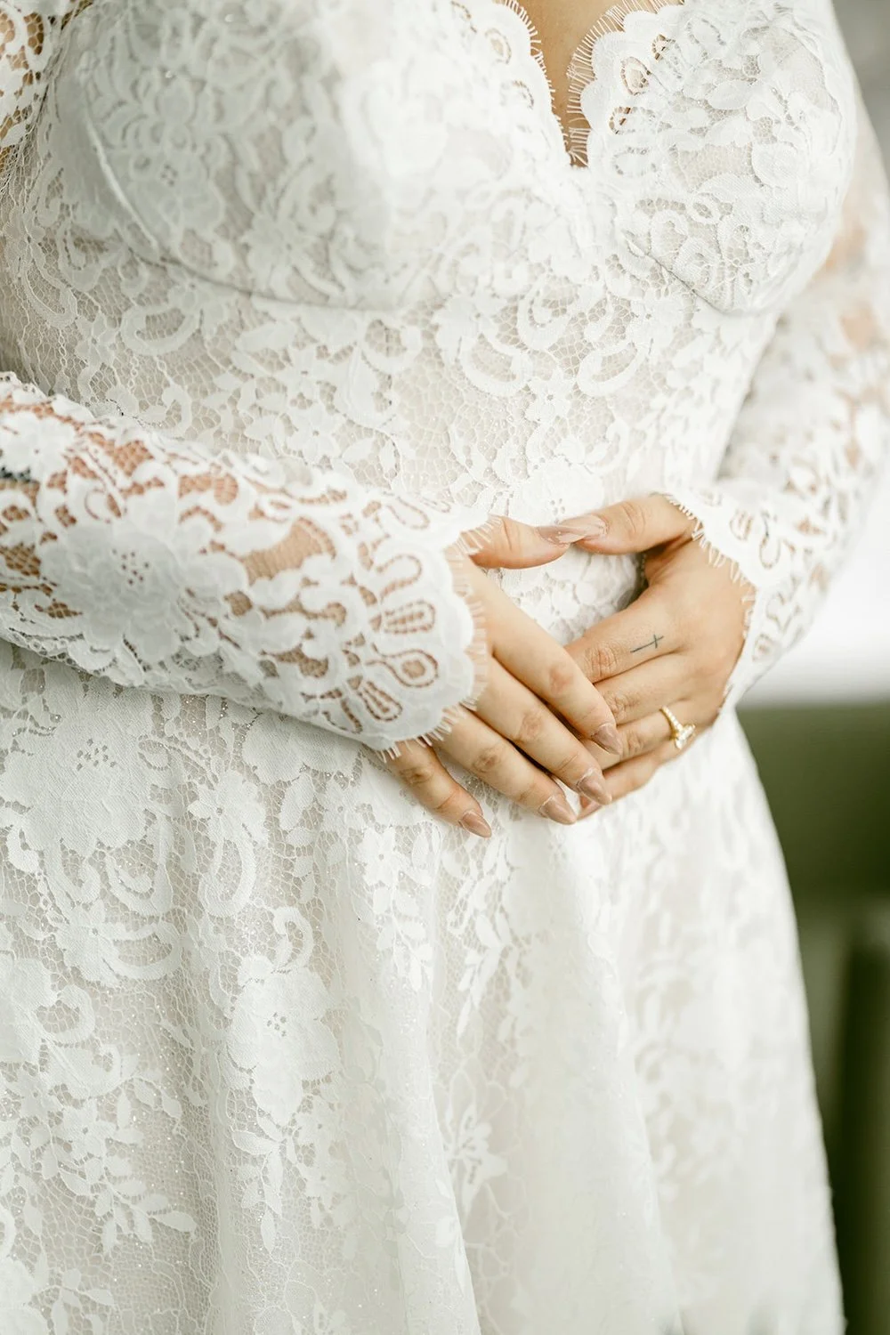 Detail photo of the brides hand's decorated with her engagement ring and lace sleeves. 