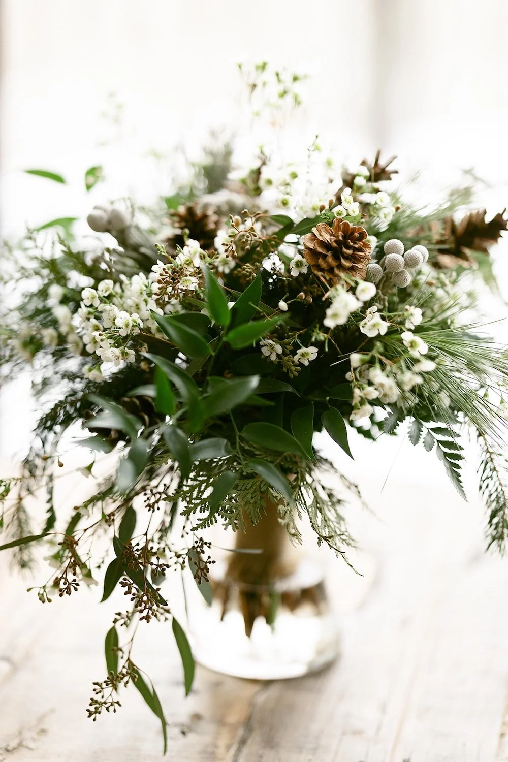 The brides bouquet resting in water decorated with pine cones and fresh greenery. 