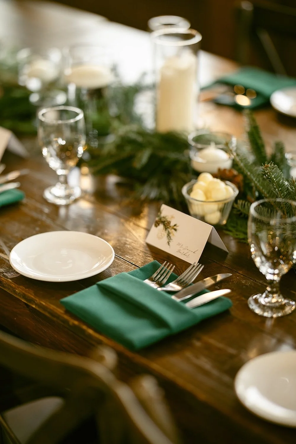 Table place setting with hunter green, evergreen branches and white candles.