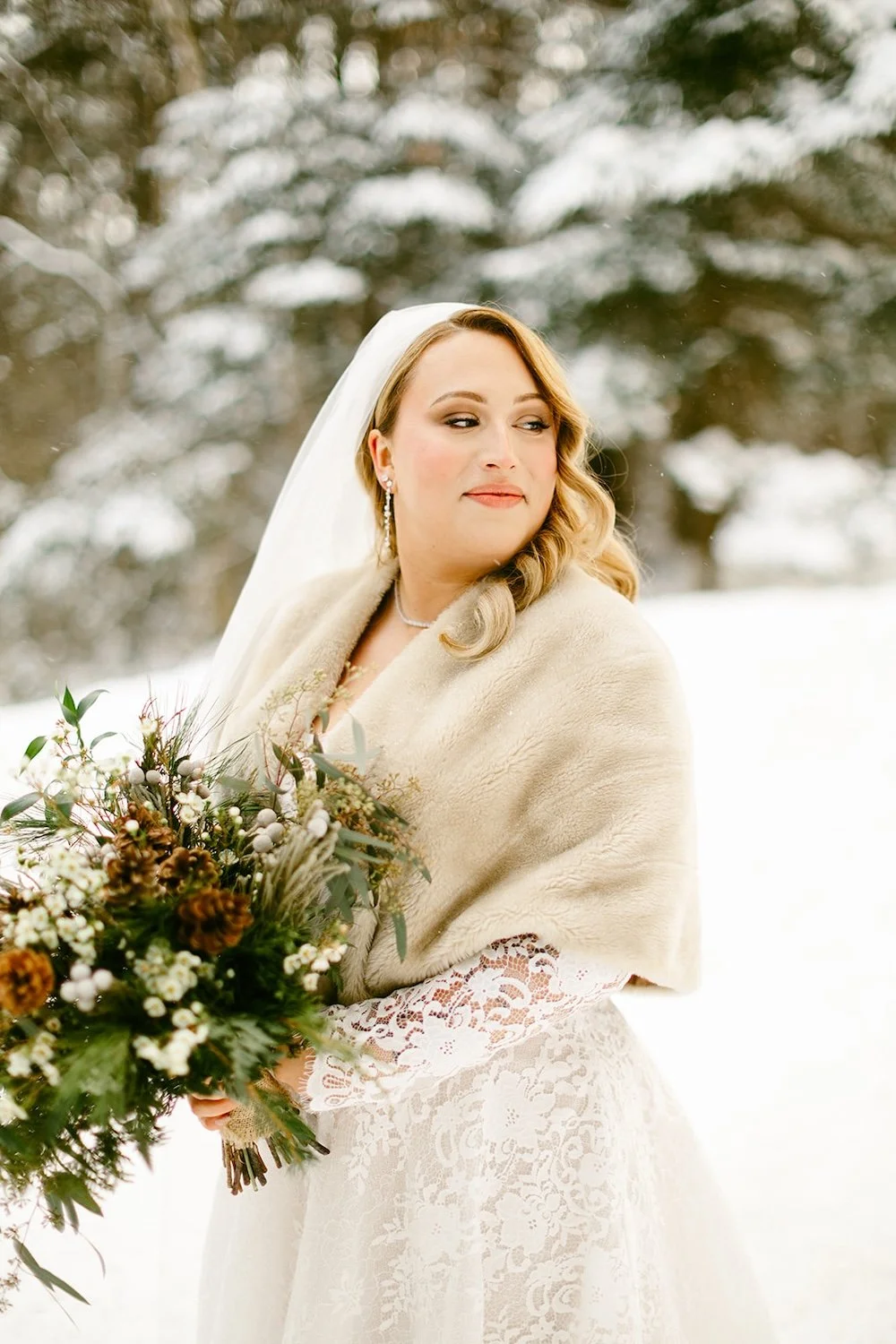 The bride poses in her wedding attire with the snow filled trail and evergreens surrounding her.
