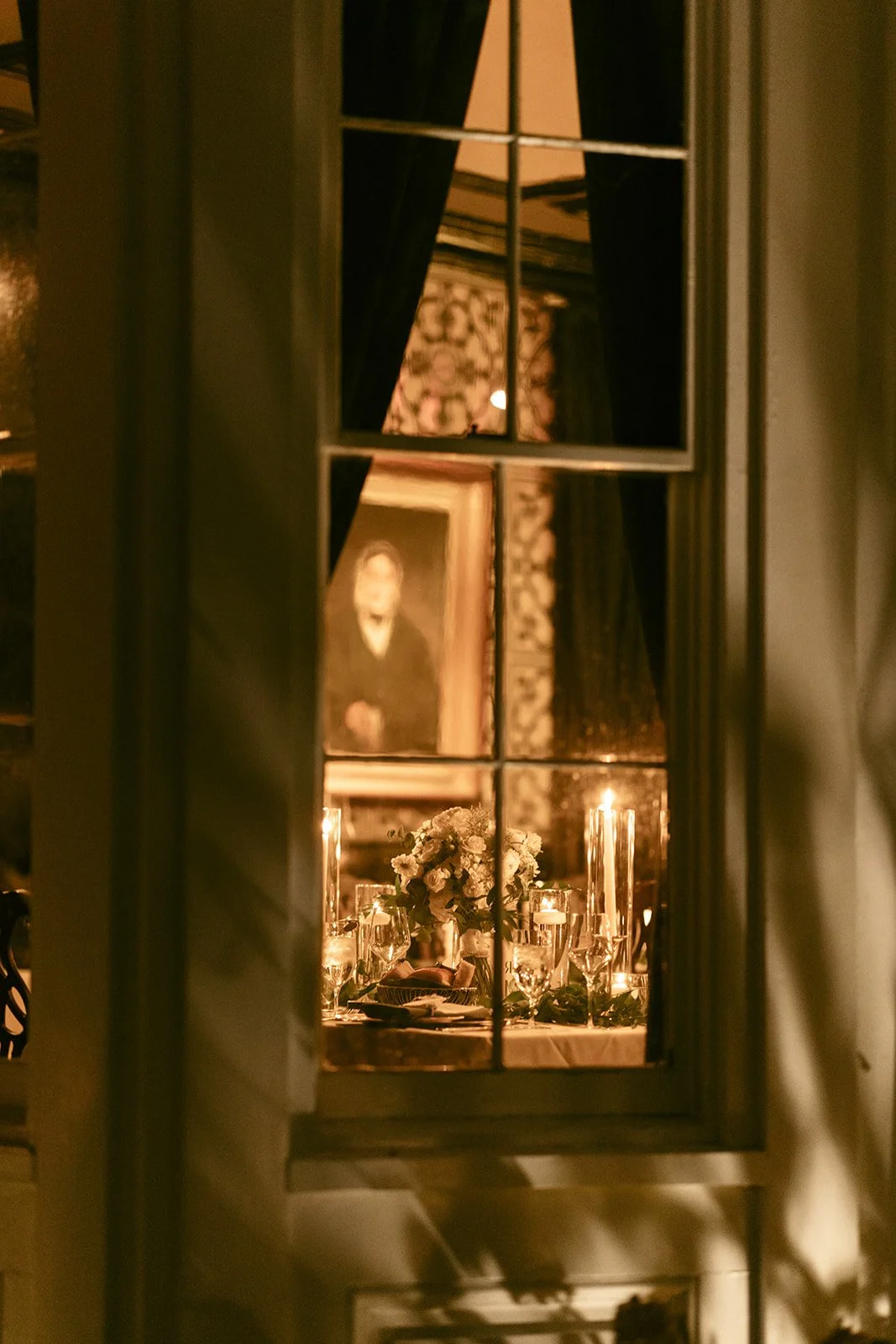 The Jones room at Inn at Taughannock Falls with long banquet tables, floral centerpieces, and candlelight, featuring a chandelier and a portrait on a patterned wall.