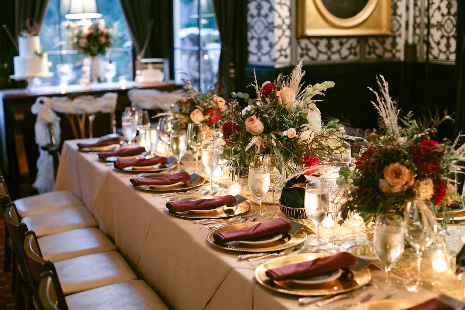 The Jones room at Inn at Taughannock Falls with long banquet tables, floral centerpieces, and candlelight, featuring a chandelier and a portrait on a patterned wall.