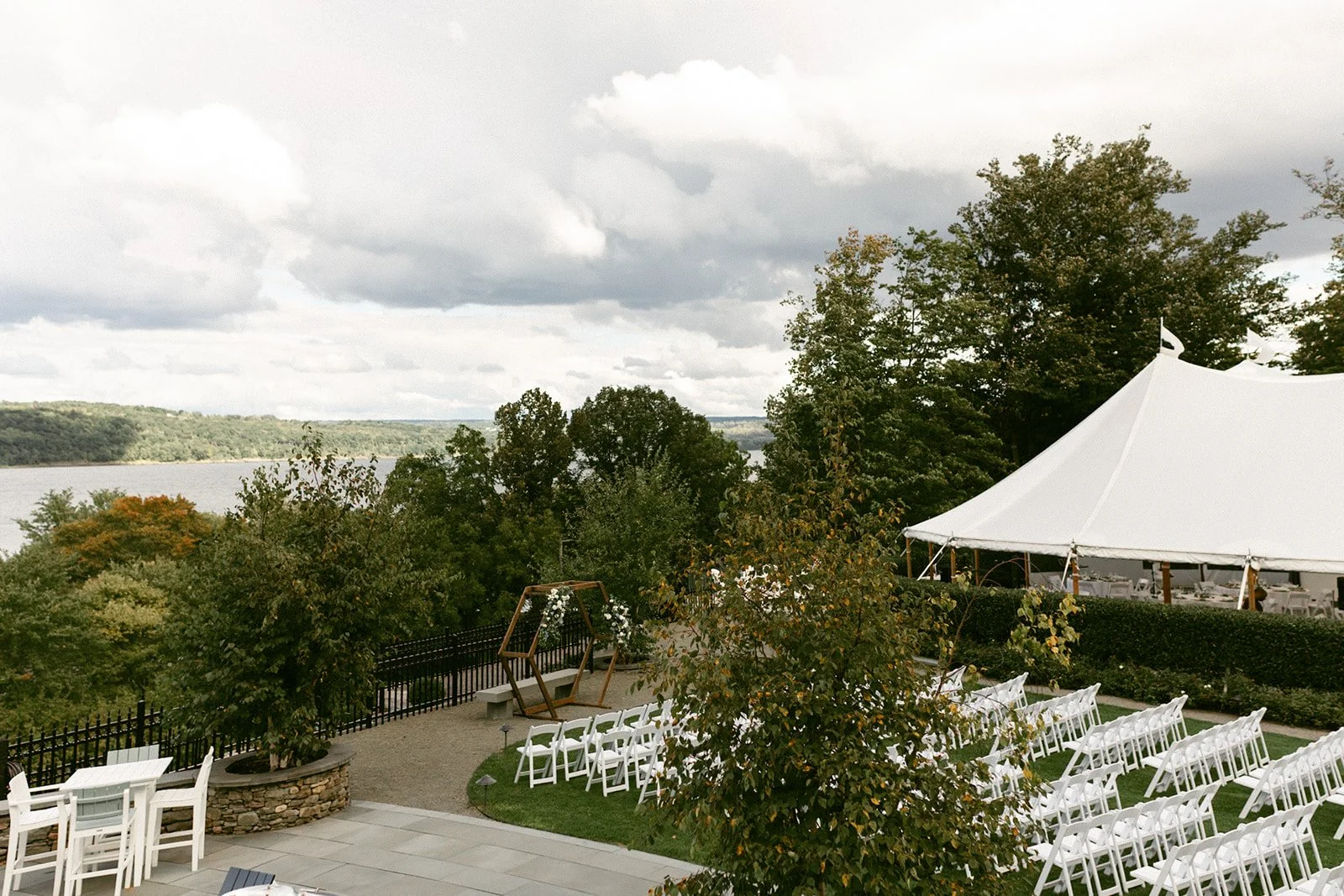 An outdoor wedding ceremony with guests seated on white chairs, a couple at the altar, officiant, and bridal party, with trees and hills in the background at for a Inn at Taughannock Falls Wedding