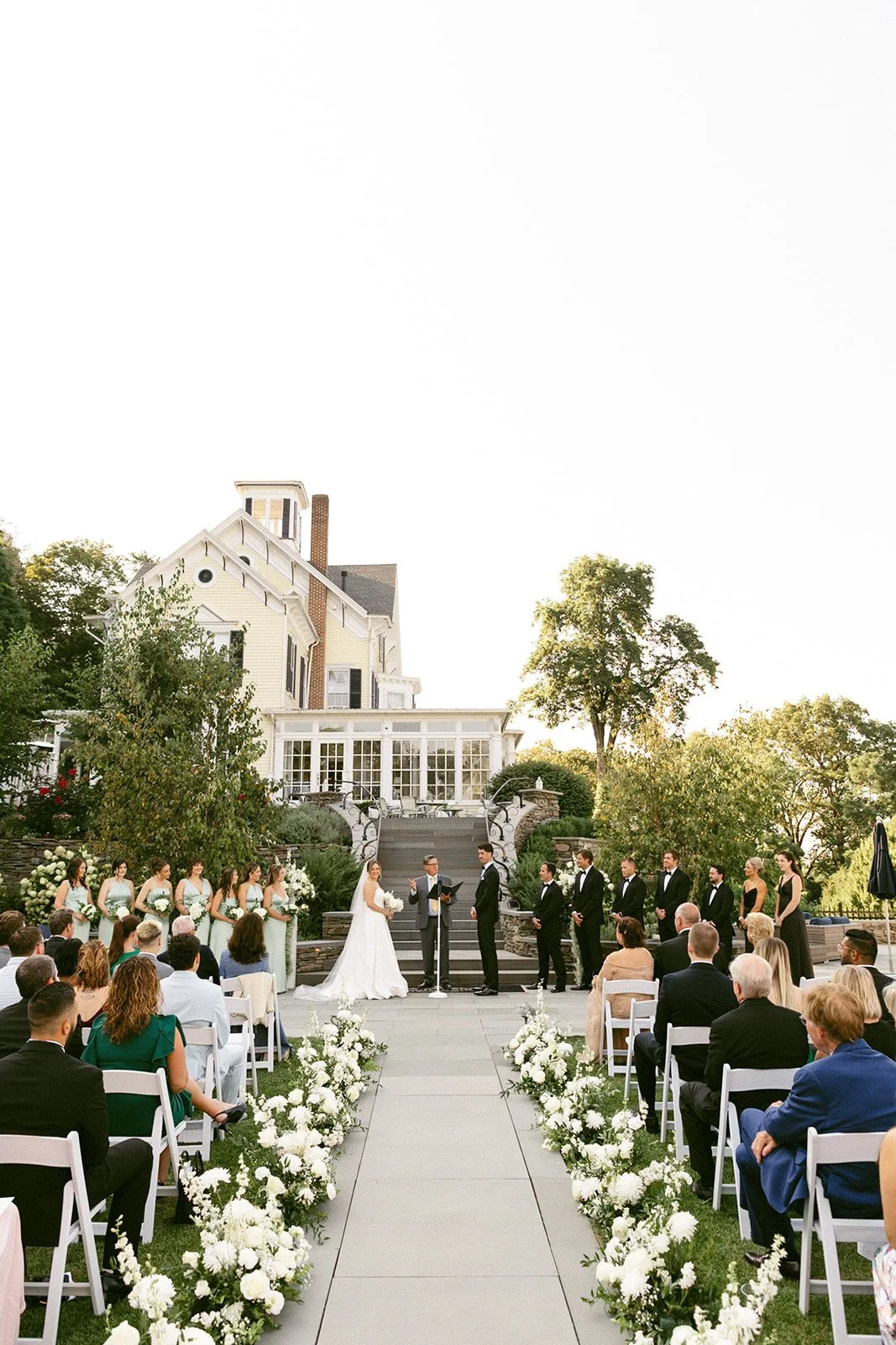 An outdoor wedding ceremony is taking place in front of a large white tent, with guests seated and a couple standing at the altar for an Inn at Taughannock Falls Wedding