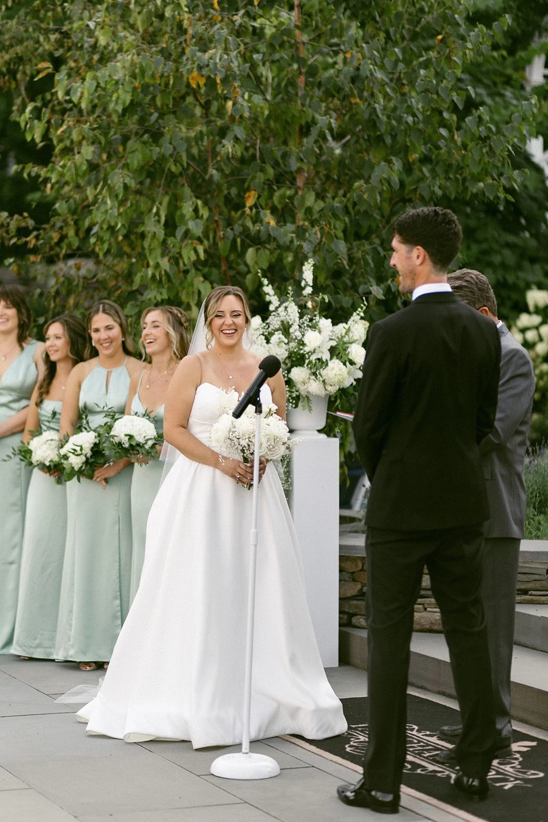 An outdoor wedding ceremony is taking place in front of a large white tent, with guests seated and a couple standing at the altar for an Inn at Taughannock Falls Wedding
