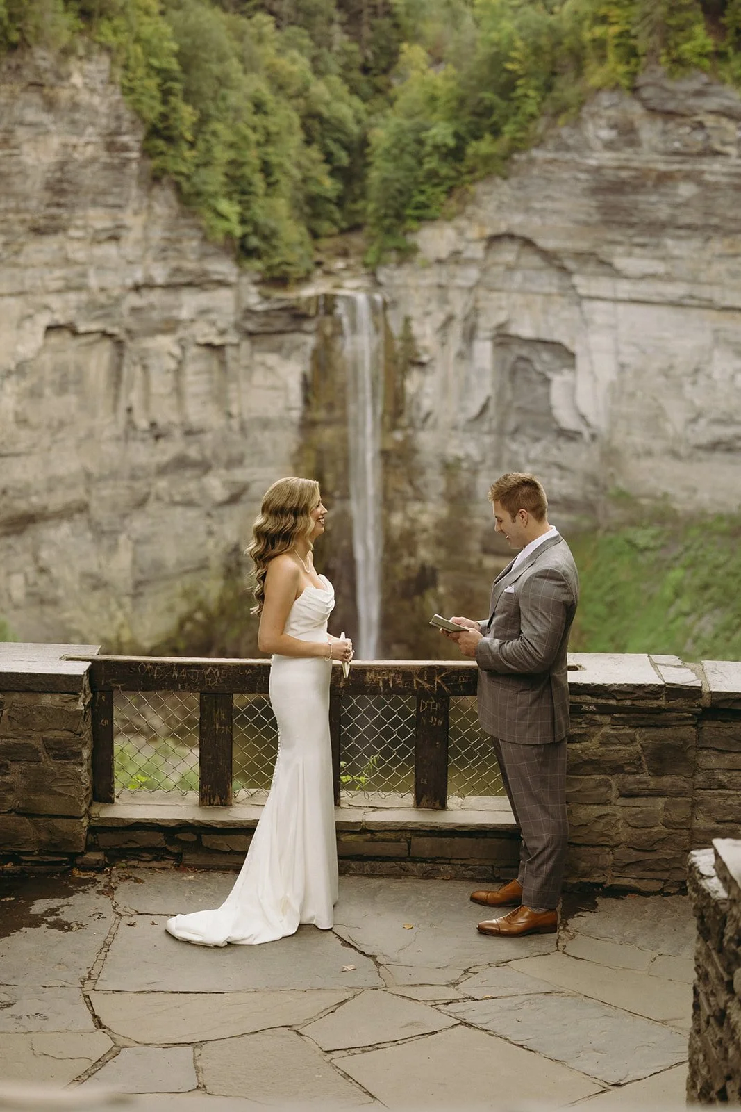 A bride and groom stand on a stone terrace overlooking a waterfall and cliffs for a wedding at Inn at Taughannock Falls Wedding