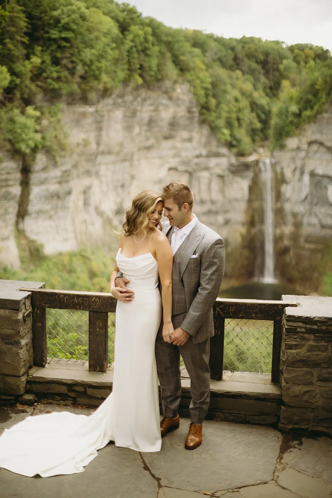A bride and groom stand on a stone terrace overlooking a waterfall and cliffs for a wedding at Inn at Taughannock Falls Wedding