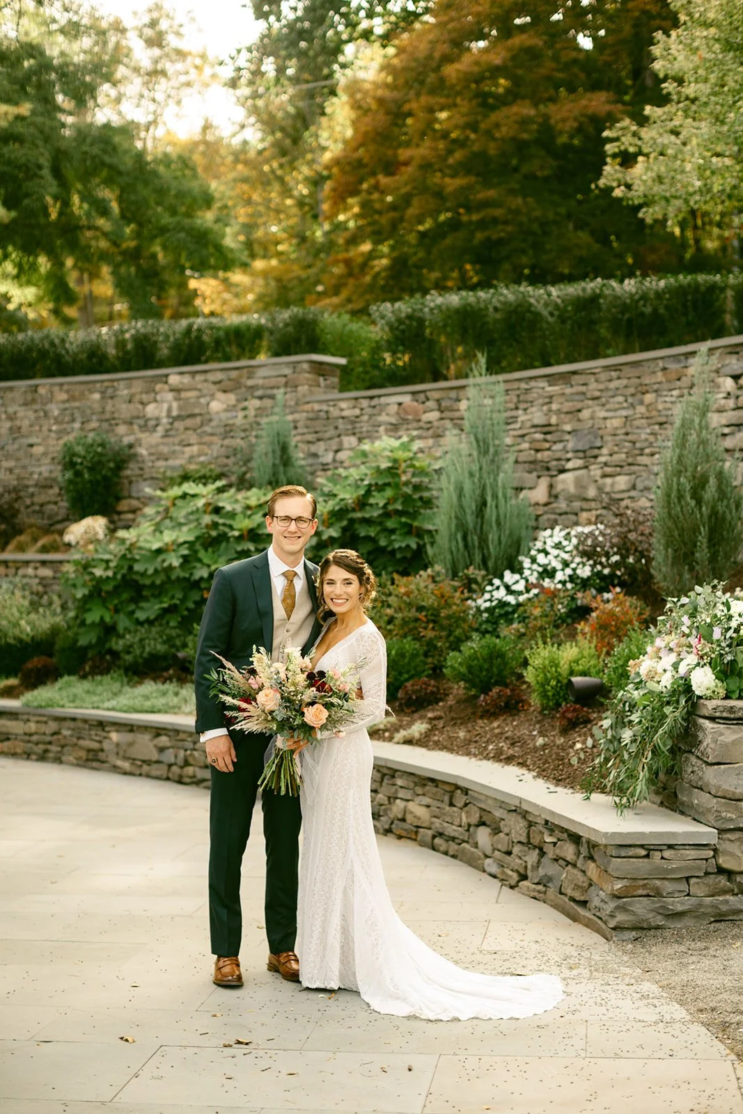A bride and groom stand holding hands on a garden path, facing each other at the Inn at Taughannock Falls
