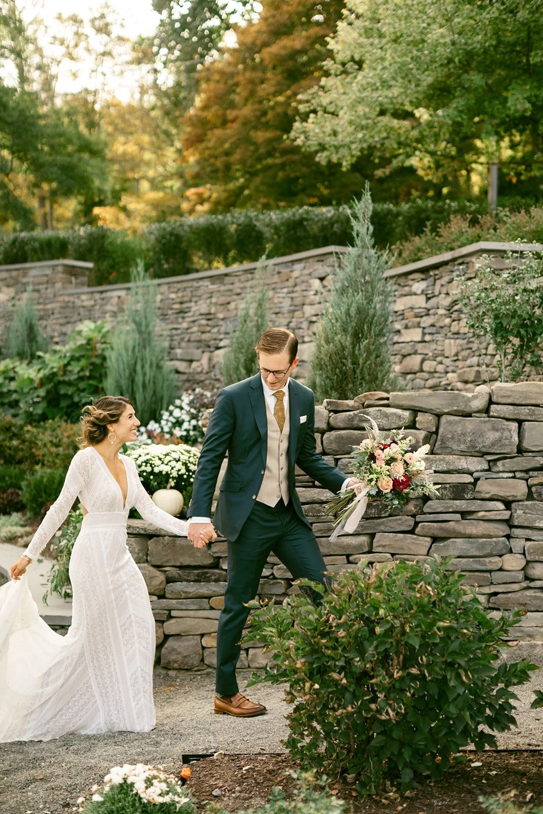 A bride and groom stand holding hands on a garden path, facing each other at the Inn at Taughannock Falls