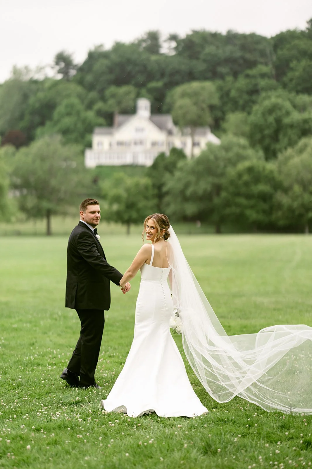 A bride and groom stand together outdoors posing for a wedding photo.