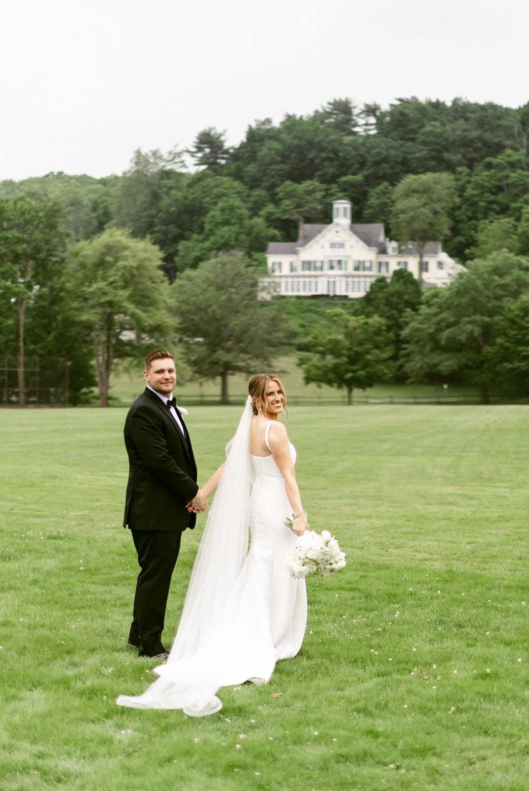 A bride and groom stand together outdoors posing for a wedding photo.