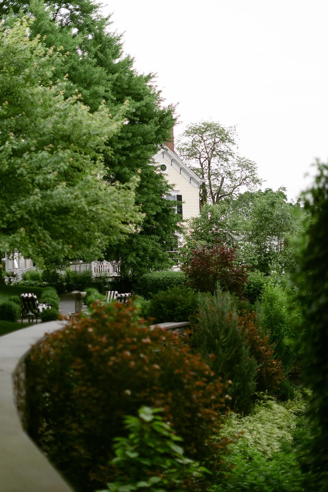Large white house with multiple gables, a sunroom, and a small tower, surrounded by greenery and a neatly manicured lawn under a clear sky at the Inn at Taughannock Falls 