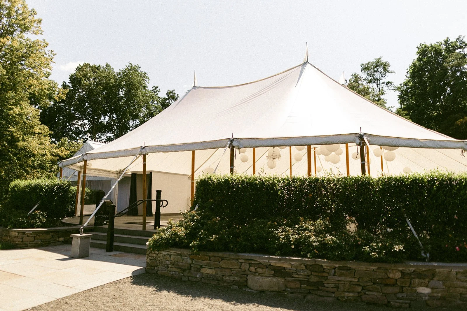 Large white house with multiple gables, a sunroom, and a small tower, surrounded by greenery and a neatly manicured lawn under a clear sky at the Inn at Taughannock Falls 