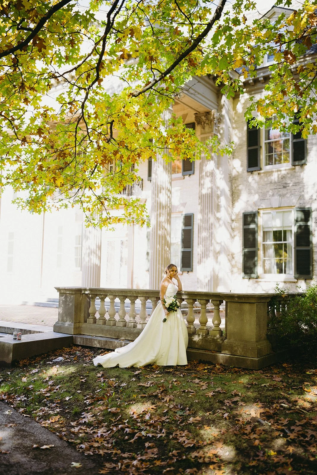 A bride and groom in formal wedding attire walk down stone steps outside a large historic building with columns at George Eastman Museum an upstate new york wedding venue 