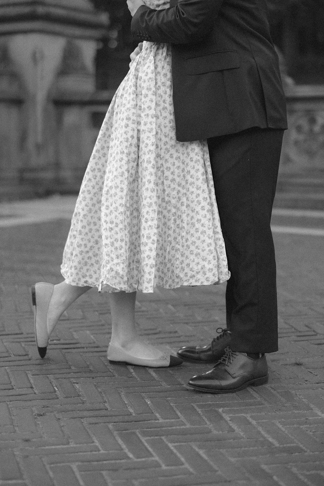A couple embraces and kisses under a stone archway with ornate detailing and a patterned wall in the background.