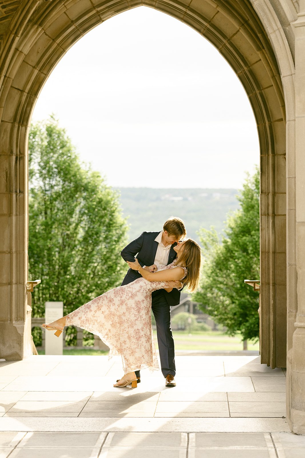 A couple stands embraced on the steps of a large stone building for outdoor engagement photos at cornell university