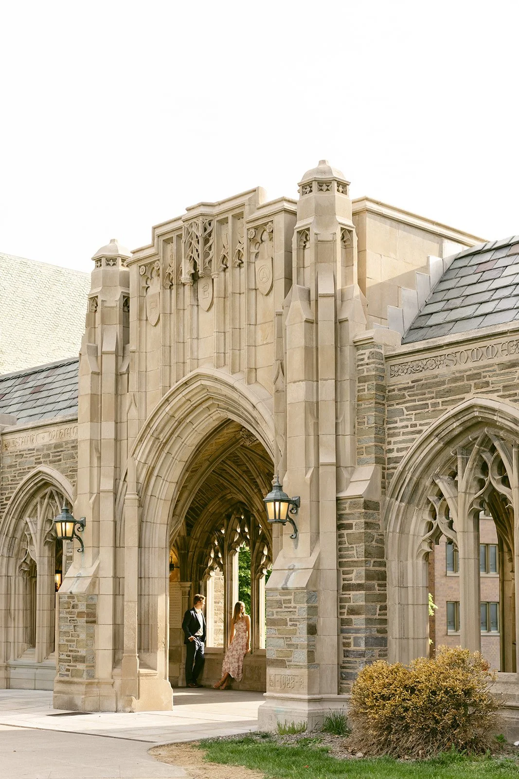A couple stands embraced on the steps of a large stone building for outdoor engagement photos at cornell university