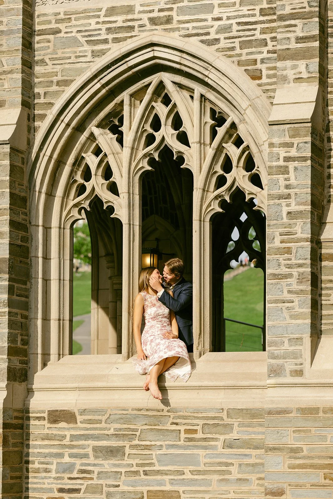 A couple stands embraced on the steps of a large stone building for outdoor engagement photos at cornell university