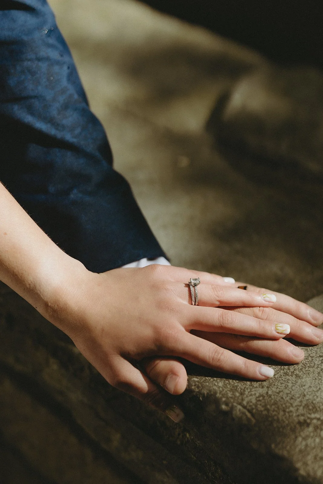 Two hands resting on a stone surface, one wearing a silver ring with a clear gemstone.
