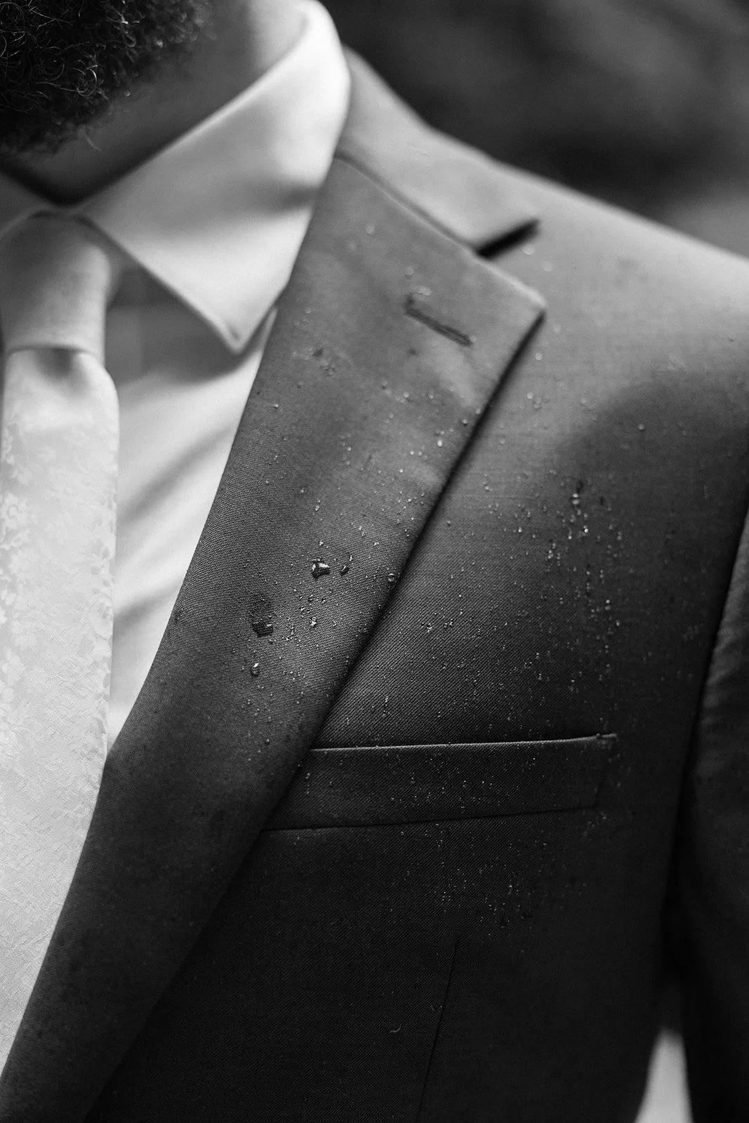 Close-up of a man’s suit jacket and tie with visible water droplets on the fabric, suggesting recent exposure to rain.