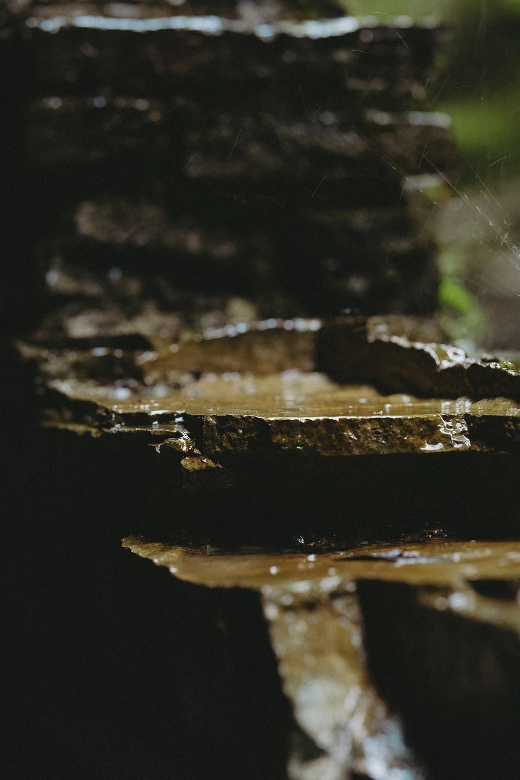 Close-up of wet, layered stone slabs outdoors, with water pooling and running over the surface, and a dark, blurred background.