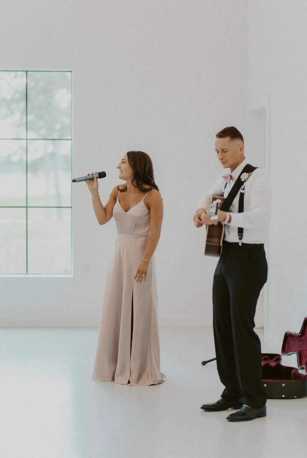 A bride and groom stand together at the altar during a wedding ceremony inside a bright, modern venue with guests and bridal party present.