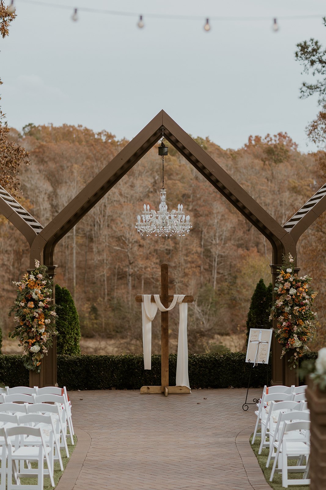 Wooden cross decorated with white flowers and greenery stands on a grassy field under a clear sky. | Christian wedding ceremony ideas