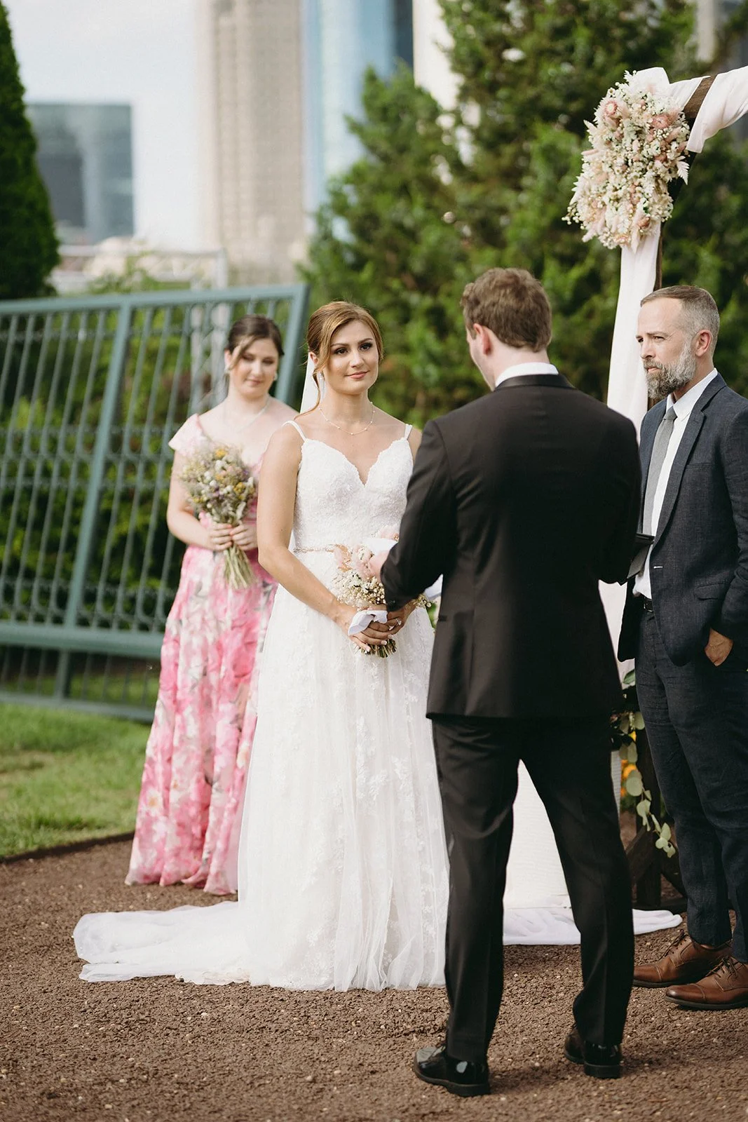 A bride and groom stand under a wedding arch outdoors with an officiant, exchanging vows for a christian wedding ceremony | Christian wedding ceremony ieas