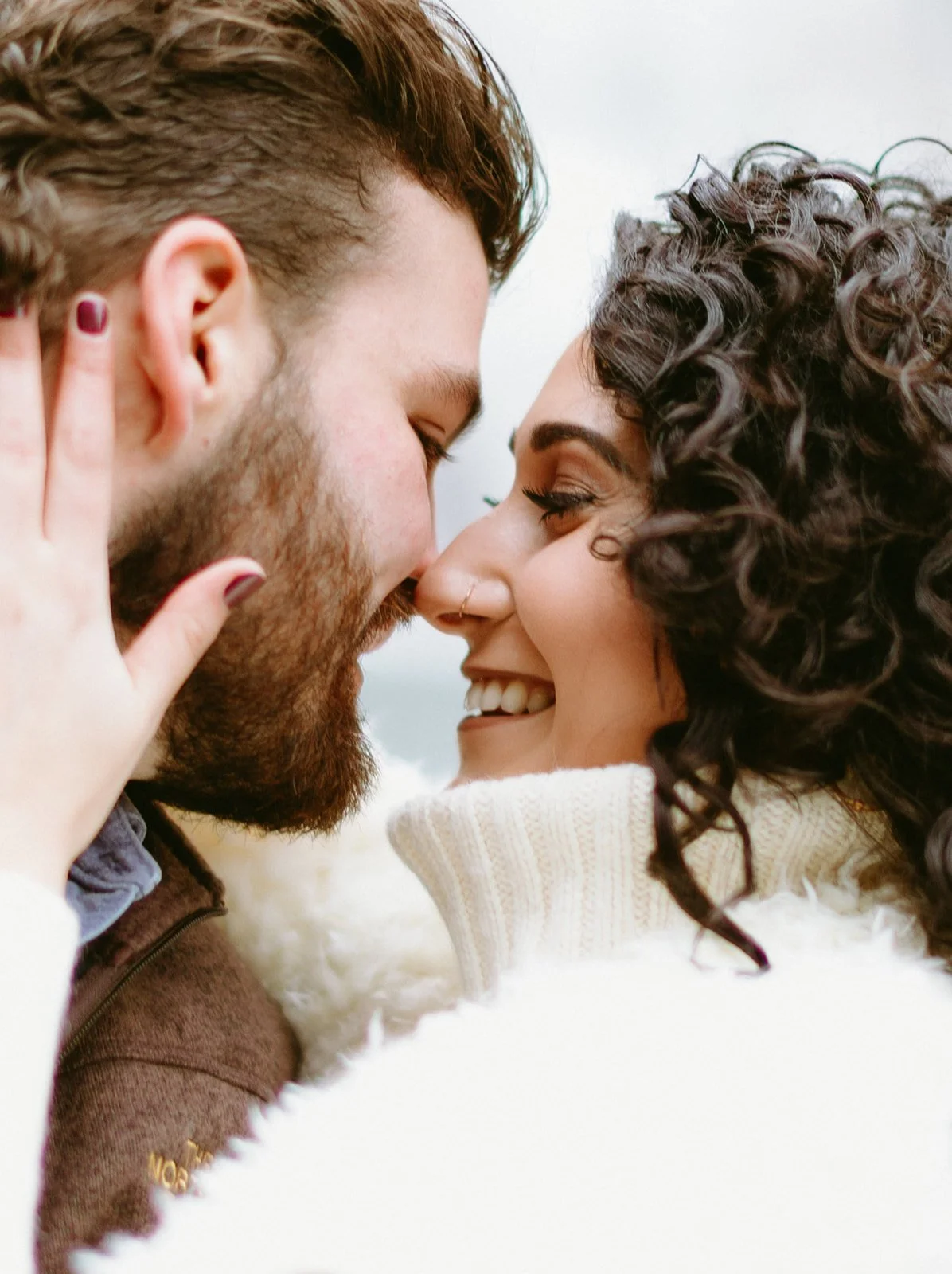 A man and a woman smiling at each other with their foreheads touching.