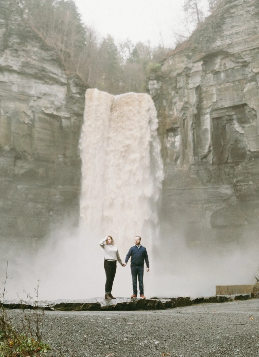 A couple holding hands while standing in front of a large waterfall.