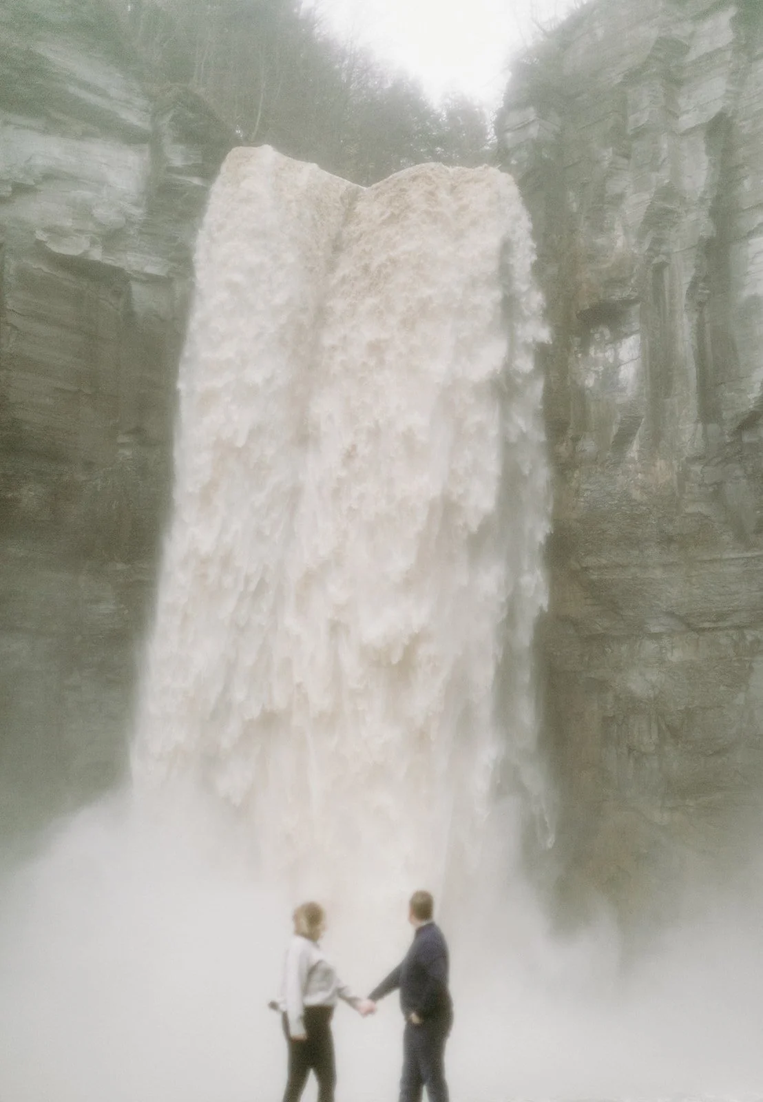 A couple holding hands while standing in front of a large waterfall.