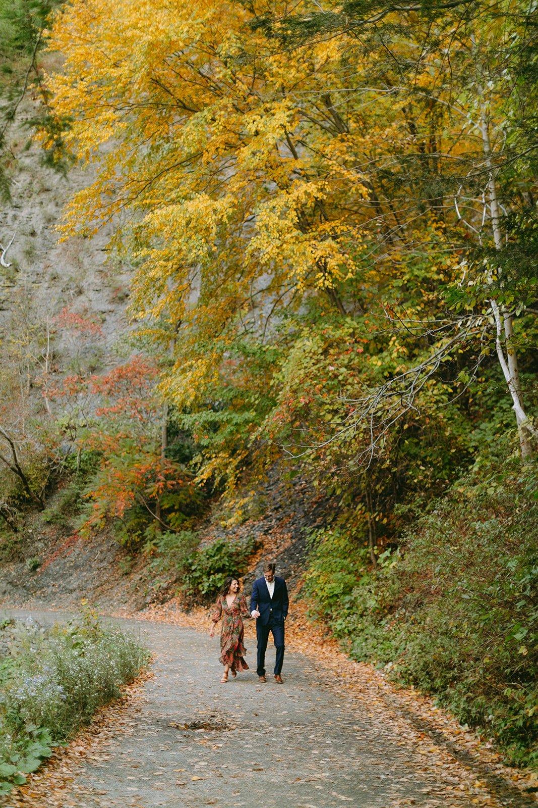 A couple walking hand-in-hand down a path lined with autumn trees.