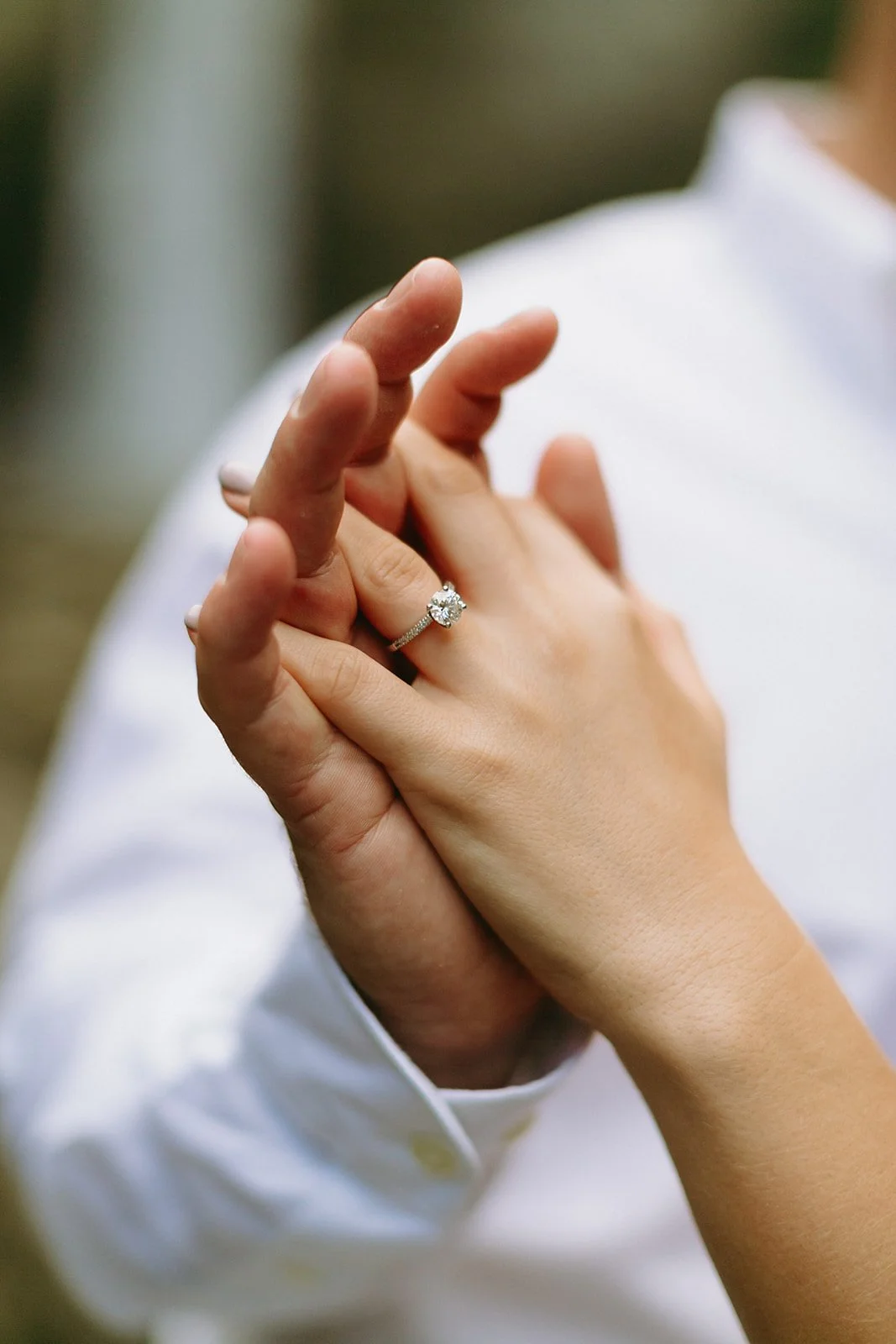 Two hands joined together, one wearing a diamond engagement ring.