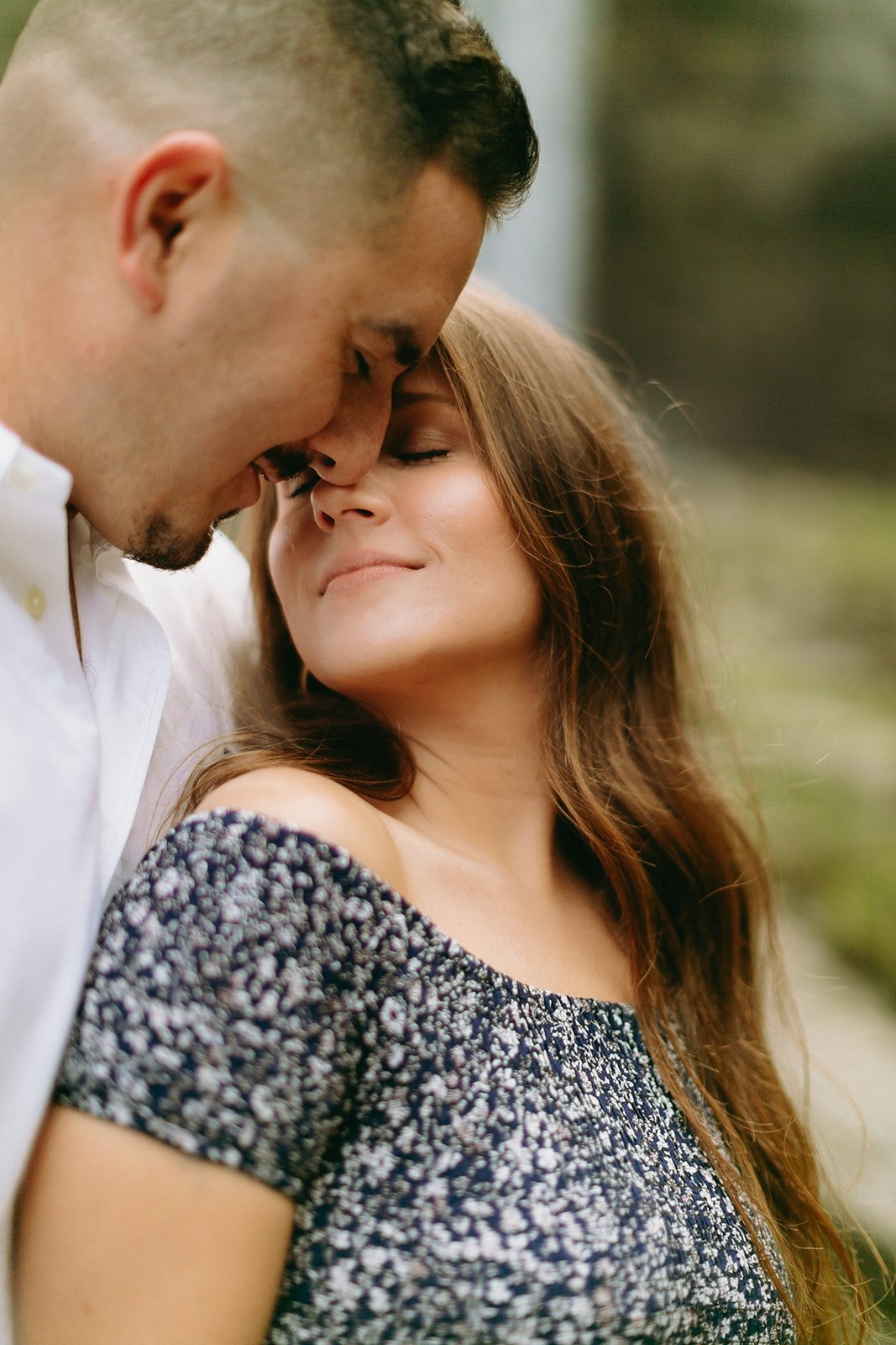 A couple standing close together, touching foreheads.
