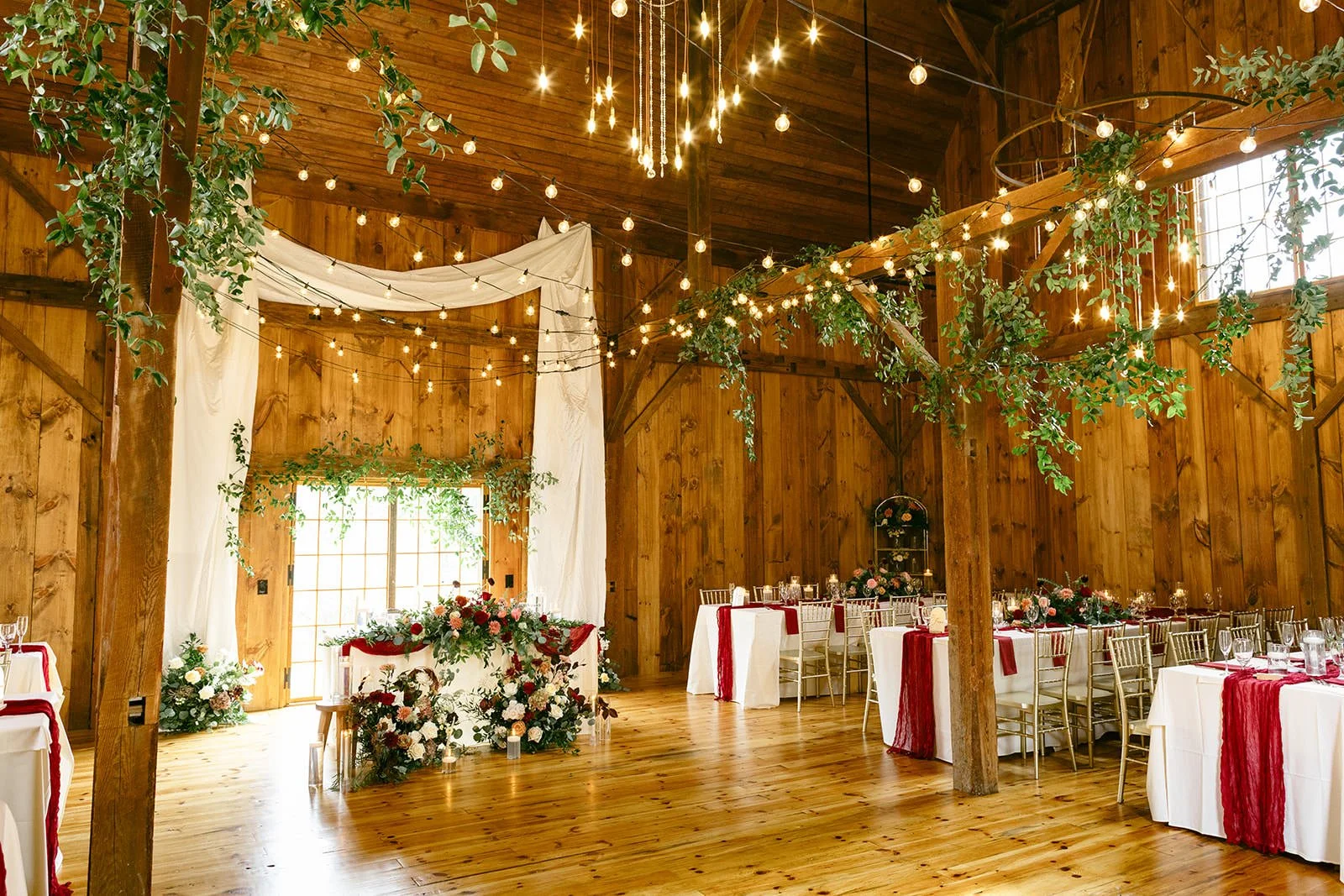 The wedding reception decorated with bright oak, sweeping greens, hanging lights and maroon and pink florals.