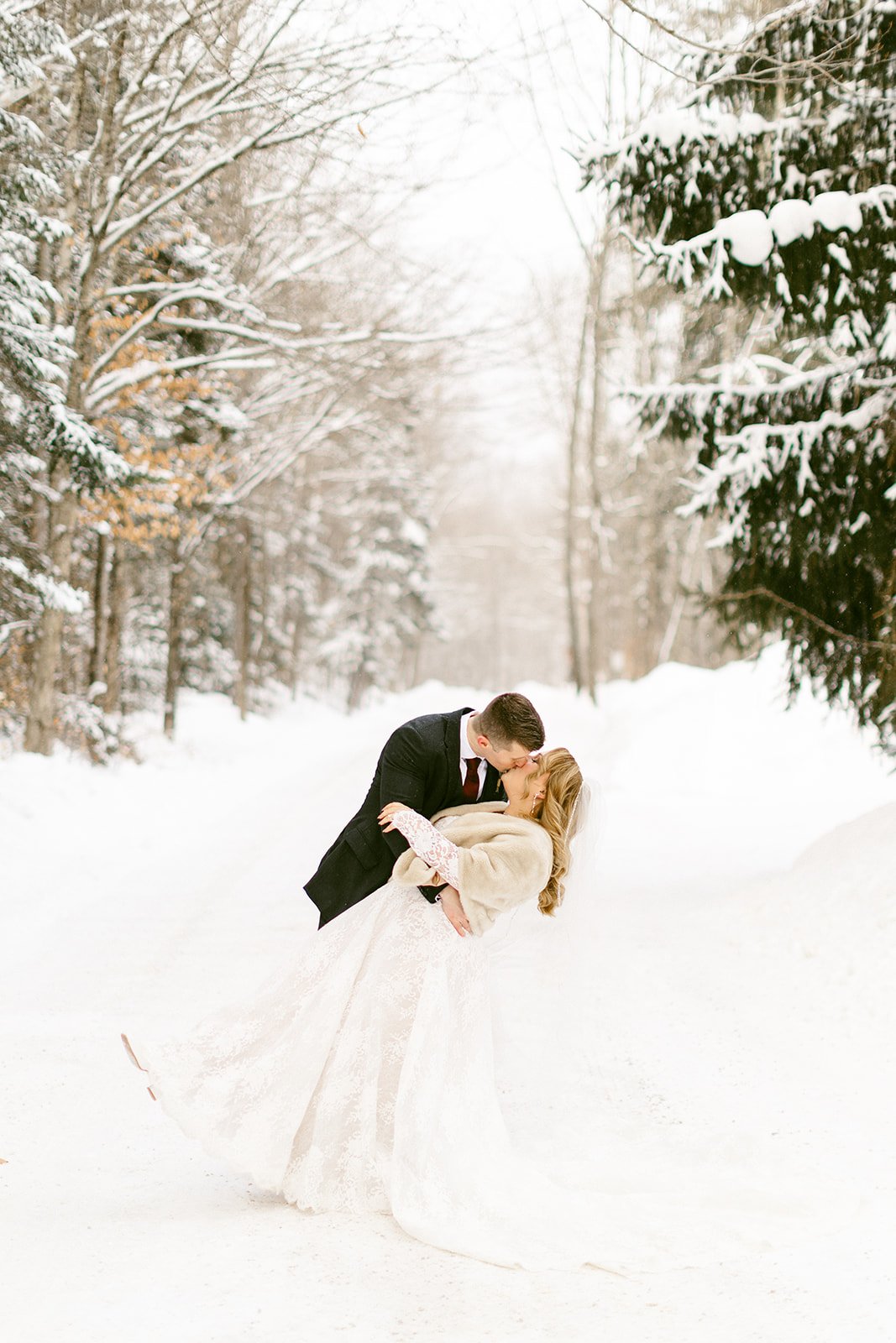 The groom dips his bride while sharing a kiss on the snowy trail.