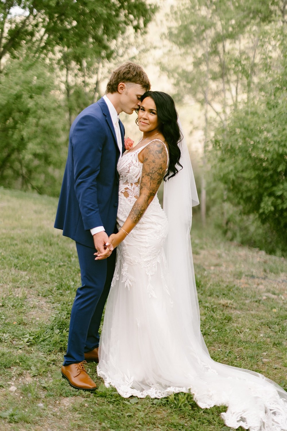Groom rests his head on his bride as they hold hands. Bride smiles toward camera.
