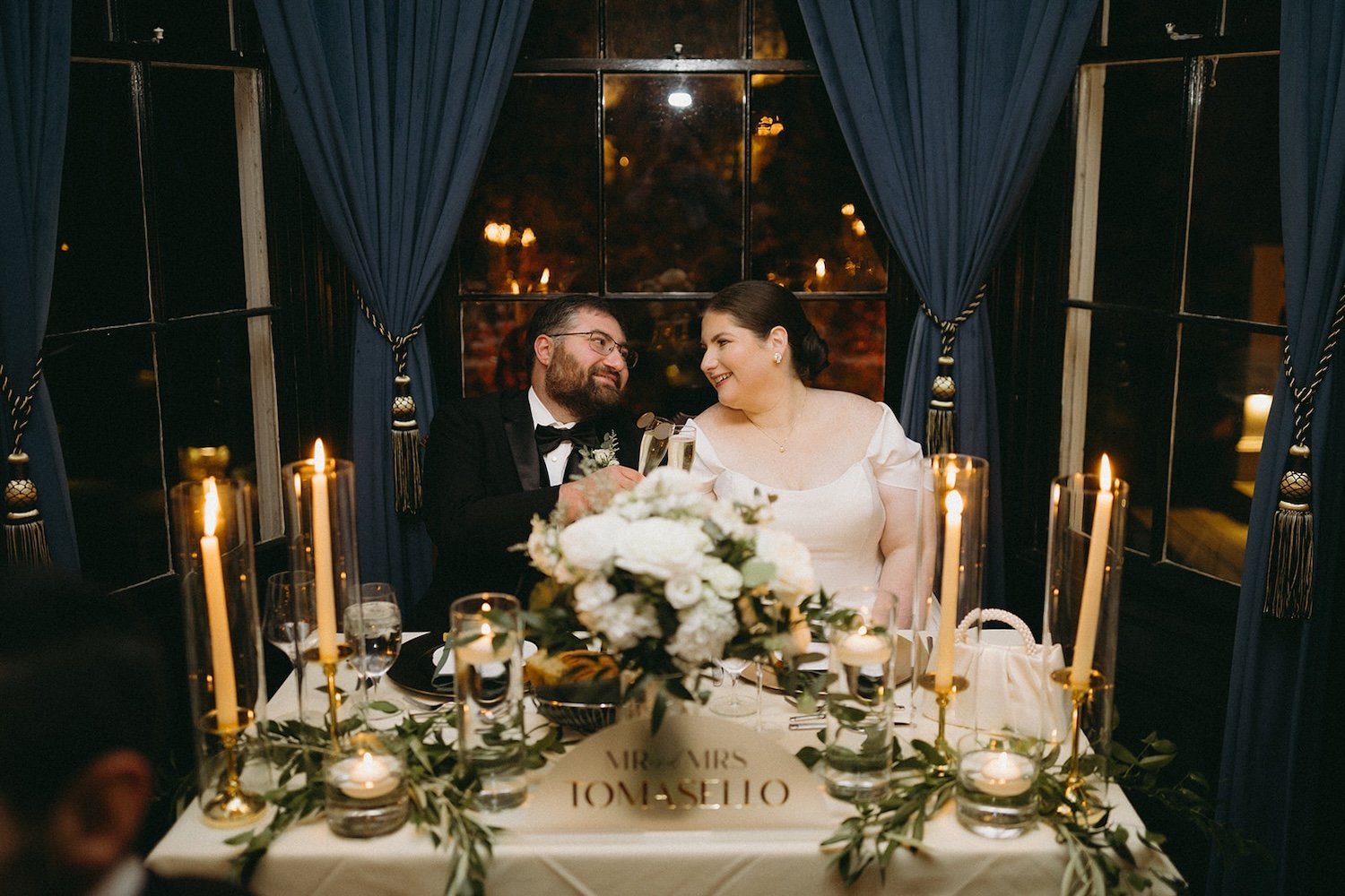 The bride and groom share a smile at their head table at the wedding reception.
