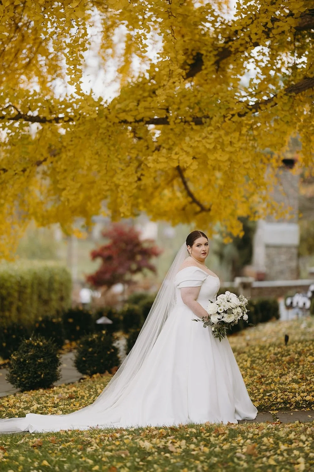 The bride stands in bridal attire with the gorgeous fall foliage surrounding her.