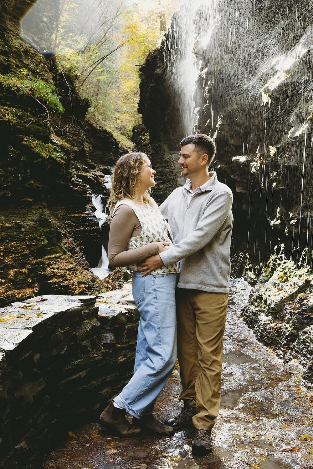 The couple hold each other close standing near the falls of the gorge. The light hits the water falling from the rocks ever so perfectly.