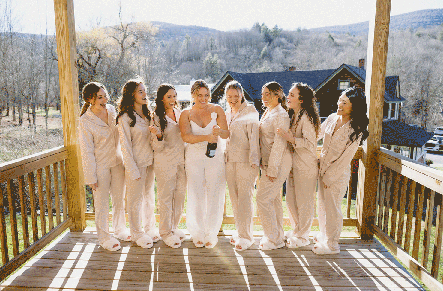 The bride and her bridal party stand on the deck popping a bottle of champagne.