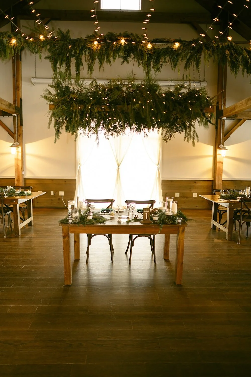 View of the head table decorated with floating evergreen branches and hanging lights.